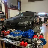 Warsztat z czarnym BMW E92, częściami zawieszenia i narzędziami. Lata produkcji tego modelu to 2006-2013.