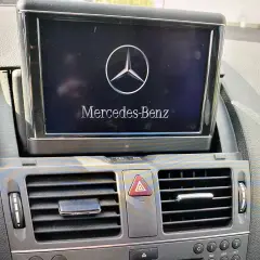 Wyświetlacz w samochodzie Mercedes-Benz z logo i napisem. Obok kratka nawiewu. Model w104.