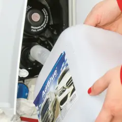 Ręce w czerwonej kurtce wlewają AdBlue z białego kanistra do wlewu paliwa samochodu.