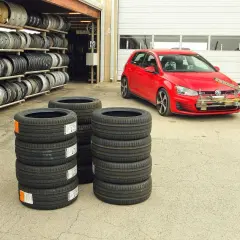 Test opon letnich 225/45 r17. Czerwony VW Golf GTI z zamontowanym sprzętem do pomiarów stoi obok stosów nowych opon.