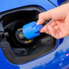 Dłoń zdejmuje niebieską nakrętkę AdBlue z wlewu paliwa samochodu.