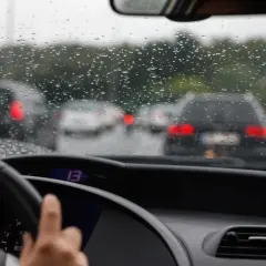 Widok z wnętrza samochodu na deszczową drogę z innymi autami i kroplami na szybie.