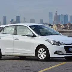 Biały Hyundai i20 zaparkowany na parkingu z widokiem na miasto w tle.
