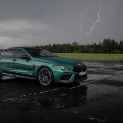 Zielony BMW M8 Competition Gran Coupé na mokrym asfalcie, z błyskawicą na burzowym niebie.