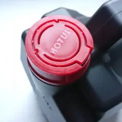 Czarne opakowanie oleju silnikowego Motul z czerwonym korkiem z logo.