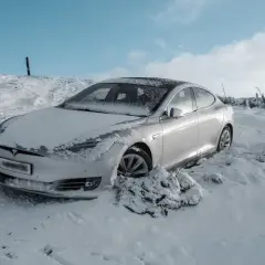 Srebrny samochód Tesla w śniegu, z widocznym logo marki.