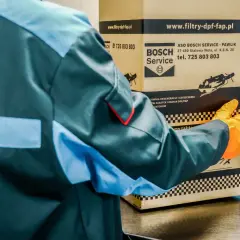 Pracownik w kombinezonie i rękawiczkach trzyma karton z logo Bosch Service.