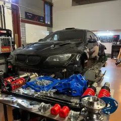 Warsztat z czarnym BMW E92, częściami zawieszenia i narzędziami. Lata produkcji tego modelu to 2006-2013.