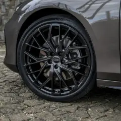 Zbliżenie na czarne felgi Audi z oponami na kamiennej nawierzchni.