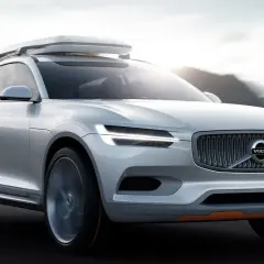 Biały Volvo XC100 z bagażnikiem dachowym jedzie po drodze, otoczony górami.