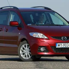 Czerwona Mazda 5 CR z młodym kierowcą za kierownicą, zaparkowana na drodze.