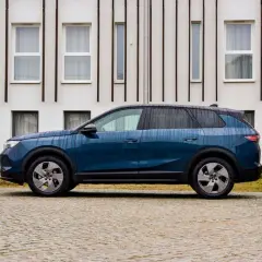 Nowoczesny, granatowy Opel hybryda stoi na brukowanym podjeździe przed minimalistycznym budynkiem.