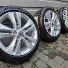 Cztery felgi aluminiowe z oponami zimowymi Bridgestone, z logo Opla, stojące na bruku.