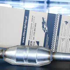 Metalowy katalizator samochodowy leży przed kartonowym opakowaniem z informacjami o usługach regeneracji.