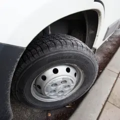 Koło busa z oponą zimową na tle białego nadwozia i chodnika.