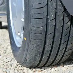 Zbliżenie na bieżnik opony samochodowej z żółtą kropką, na tle żwiru.