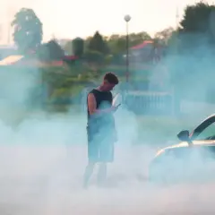 Mężczyzna w dymie z opon obok samochodu.