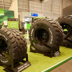 Trzy duże opony rolnicze Nokian Tyres na zielonej wykładzinie.