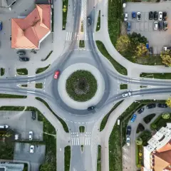Widok z lotu ptaka na rondo z samochodami i budynkami w tle.