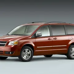 Pomarańczowy Dodge Grand Caravan z chromowanymi listwami i relingami dachowymi, gotowy na rodzinną podróż.