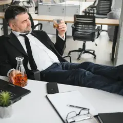 Mężczyzna w garniturze z alkoholem w ręku, zastanawia się, czy pracodawca może sprawdzać alkomatem.