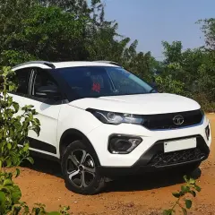 Biały Tata Nexon stoi na piaszczystej drodze, otoczony zielenią.