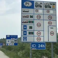 Znaki drogowe z limitami prędkości i informacją o opłatach drogowych na drodze ekspresowej.