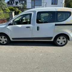 Biały Renault Dokker z żółtymi naklejkami na tylnej części, zaparkowany na ulicy.