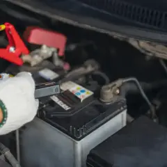 Rękawica w białej rękawiczce podłącza prostownik do akumulatora samochodowego, aby rozpocząć ładowanie.