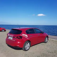 Czerwony fiat tipo sedan zaparkowany nad błękitnym jeziorem.