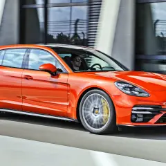 Pomarańczowe porsche 971 Sport Turismo pędzi po drodze, kierowca w okularach przeciwsłonecznych za kierownicą.