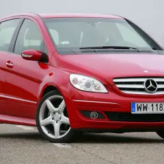 Czerwony Mercedes W245 na drodze, z widocznym grillem i reflektorami.
