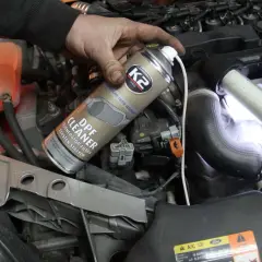 Ręka trzymająca puszkę preparatu do czyszczenia DPF w silniku samochodu.