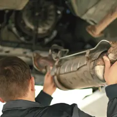 Mechanik trzymający pod samochodem zardzewiały element układu wydechowego, prawdopodobnie DPF.