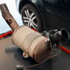 Filtr DPF na stole warsztatowym, z widocznym elementem wydechowym i złączem elektrycznym.