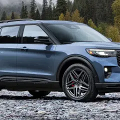 Niebieski Ford Explorer Sport ST na kamienistej plaży, z jesiennym lasem w tle.