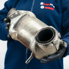 Mechanik w rękawiczkach trzyma katalizator, element układu wydechowego. Rozważasz wyprogramowanie DPF?