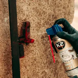 Ręka w czarnej rękawiczce aplikuje smar K2 LT-43 na metalowy element.