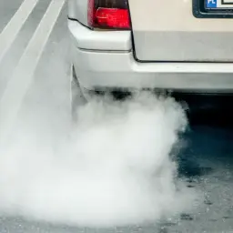 Z rury wydechowej samochodu wydobywa się gęsty, biały dym, który rozprzestrzenia się na drodze.