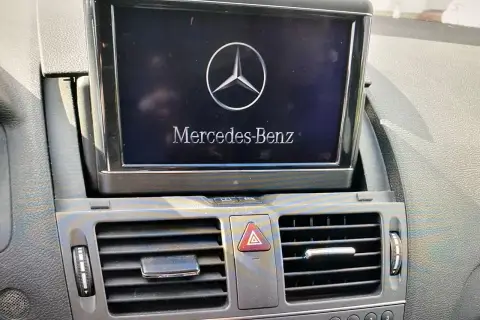 Wyświetlacz w samochodzie Mercedes-Benz z logo i napisem. Obok kratka nawiewu. Model w104.