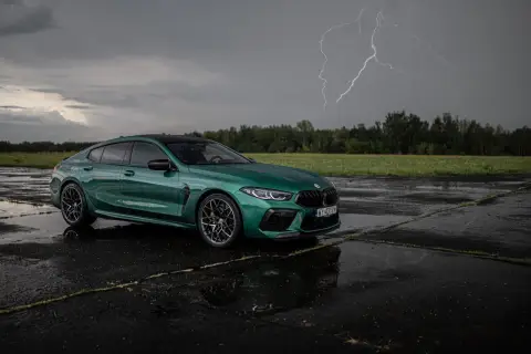 Zielony BMW M8 Competition Gran Coupé na mokrym asfalcie, z błyskawicą na burzowym niebie.