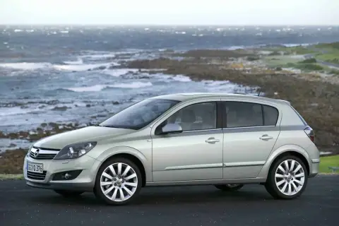 Srebrny Opel Astra H, popularny model z lat produkcji 2004-2009, zaparkowany na tle skalistego wybrzeża i wzburzonego morza.