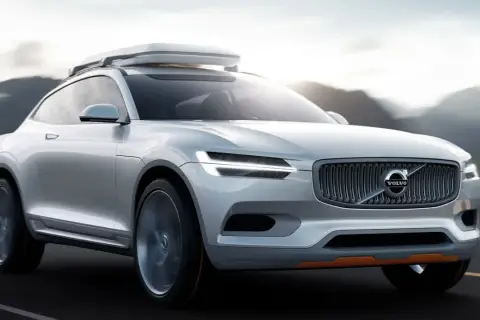 Biały Volvo XC100 z bagażnikiem dachowym jedzie po drodze, otoczony górami.