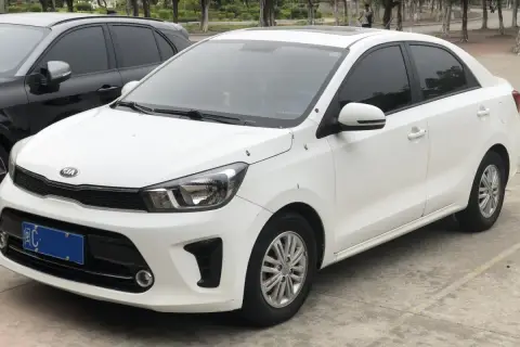 Biały sedan Kia Pegas z przyciemnianymi szybami zaparkowany obok czarnego SUV-a.