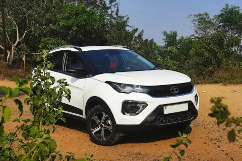 Biały Tata Nexon stoi na piaszczystej drodze, otoczony zielenią.