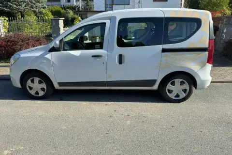 Biały Renault Dokker z żółtymi naklejkami na tylnej części, zaparkowany na ulicy.