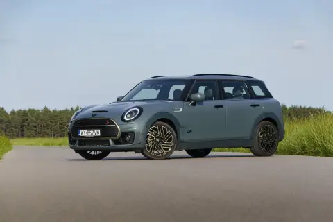 Szary Mini Clubman F54 z napędem ALL4 na tle lasu i łąki.