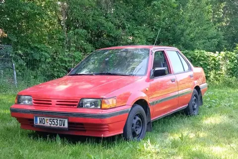 Czerwony Nissan Sunny N13, klasyk z lat 80., stoi na trawie, gotowy na nowe przygody.