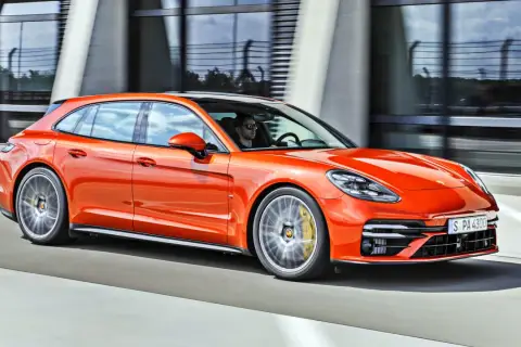 Pomarańczowe porsche 971 Sport Turismo pędzi po drodze, kierowca w okularach przeciwsłonecznych za kierownicą.