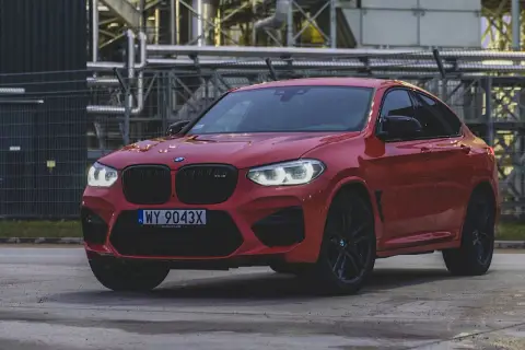 Czerwone BMW X4 z czarnymi felgami i grillem, zaparkowane przed przemysłowym budynkiem.
